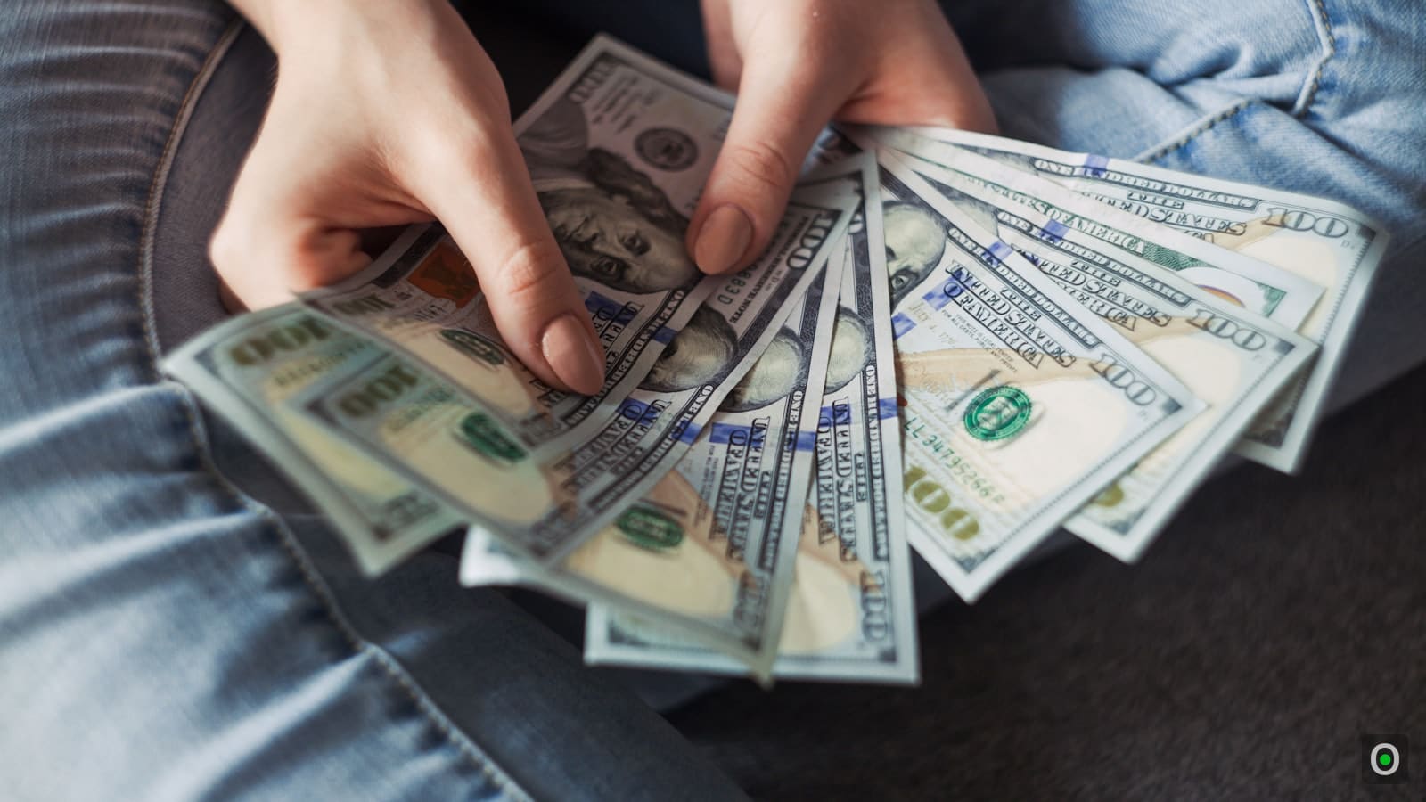 Hands fanning out several hundred-dollar bills, representing savings earning interest